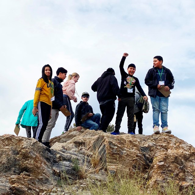 group of young people standing atop a rock outcrop, one with arm raised in victory pose