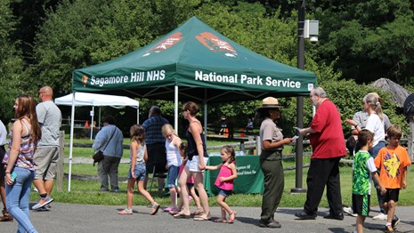A crowd walks past a tent that says 