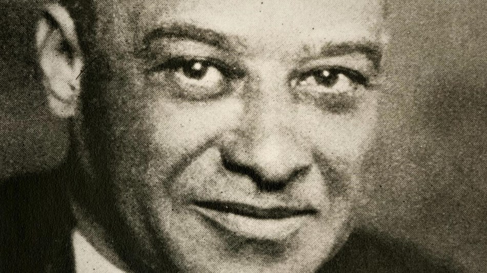 An African American man wearing a dark jacket and tie.