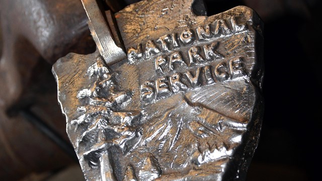 A metal arrowhead with raised mountain, trees, buffalo and National Park Service.