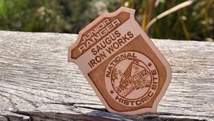 A wooden badge that says "Saugus Iron Works Junior Ranger"