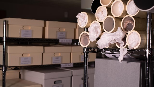 Different sized boxes and tubes on shelves filled with artifacts.