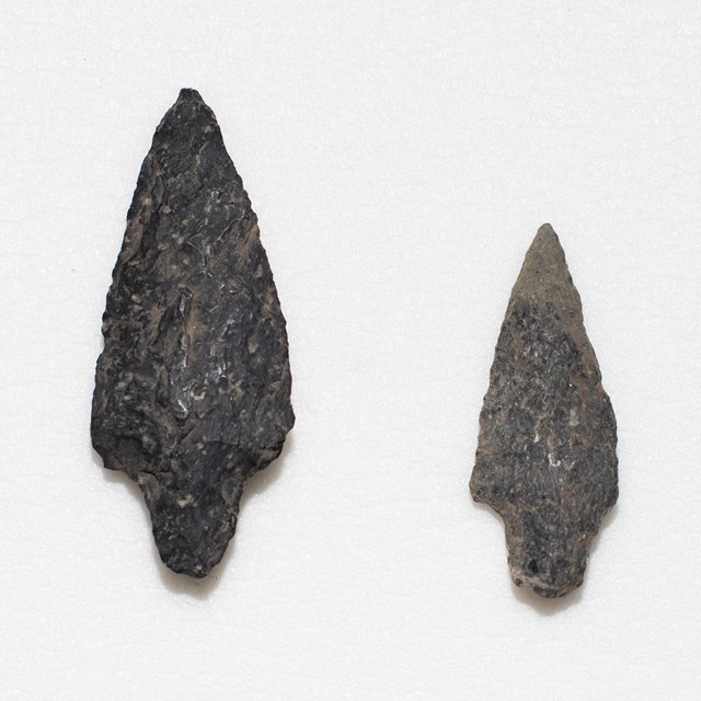 Two gray triangular shaped projectile points with a rounded, tapered stem.