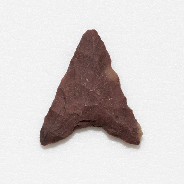 Reddish pink triangular projectile point with concave base.