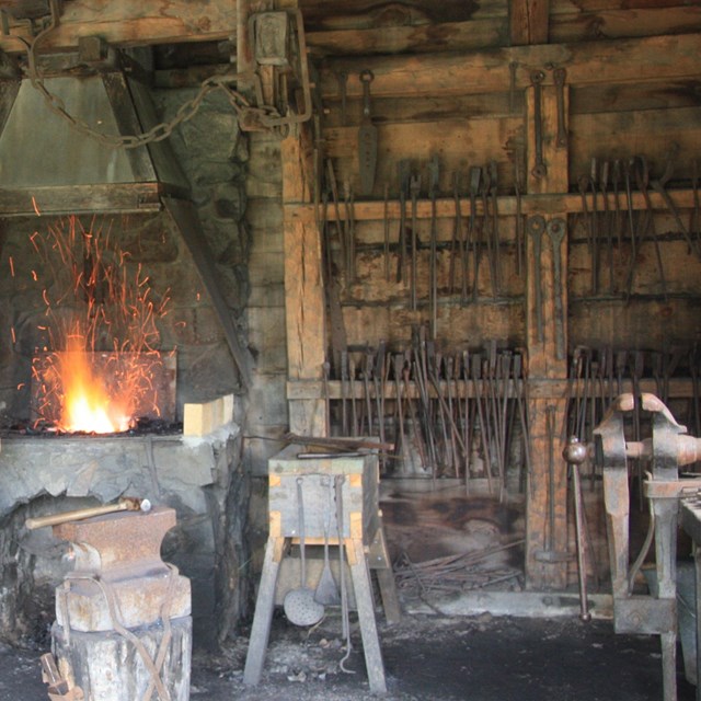 fire burns and sparks in raised stone fireplace with various tools for ironmaking nearby
