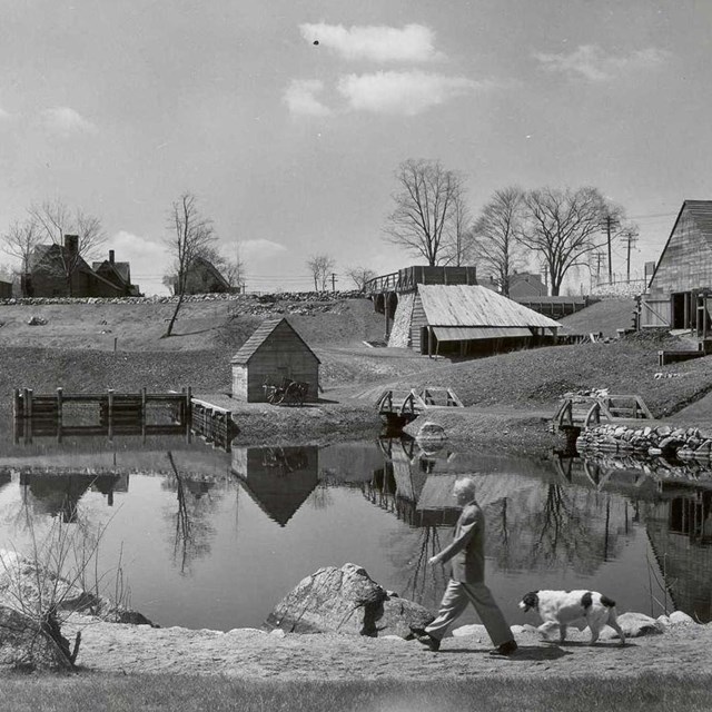 Black and white photograph of a man in suit walking a dog in front of the Iron Works