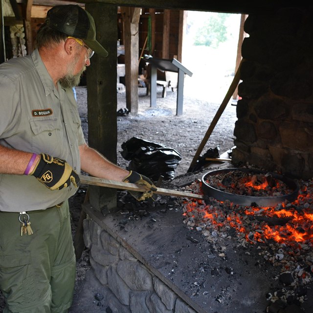 uniformed park ranger with metal rod poking hot coals in a forge.