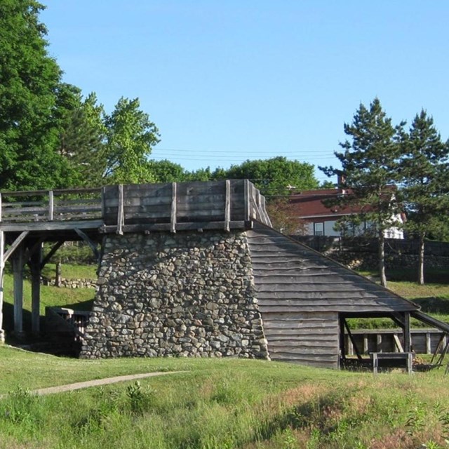 A stone furnace topped by a wooden bridge and open-air shed on bottom.
