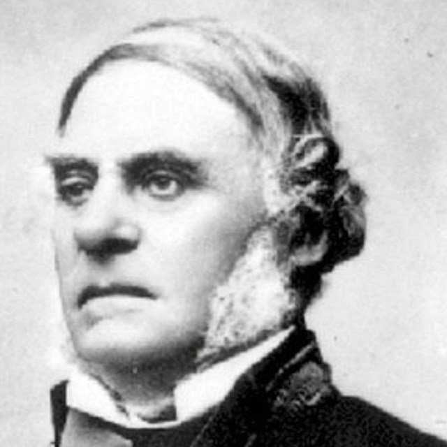 Black and white headshot of a man with Mutton Chops