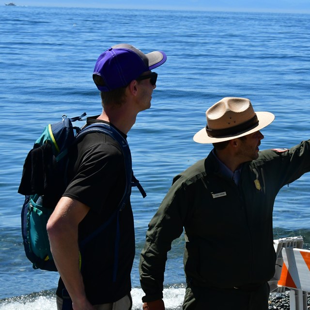 A park ranger points in the distance at something on a beach