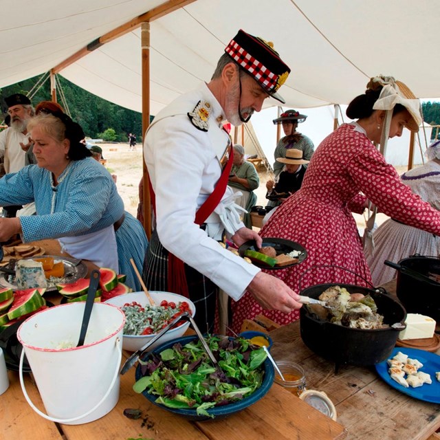 Reenactors helping themselves to a buffet of historically accurate foods.