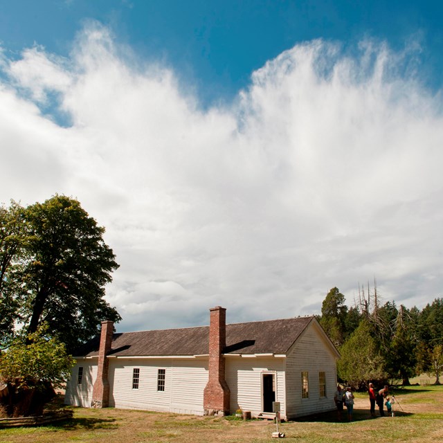 Photograph of a one story 19th century wood frame building with dramatic clouds behind it