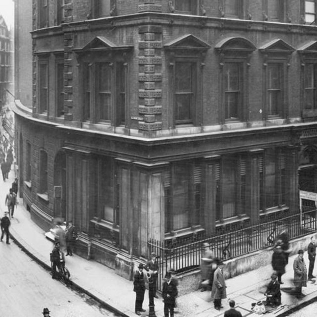 Black and white photo of an ornate building with many people passing by