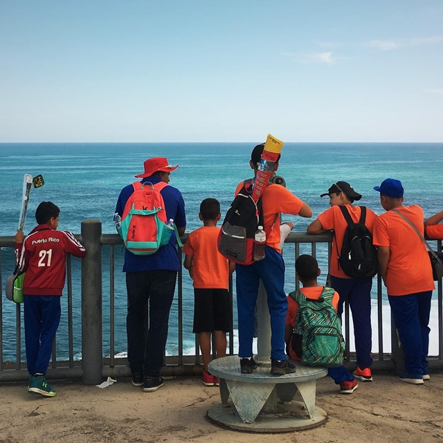 A teacher looks out into the ocean from El Morro's 4th level with his group of students. 