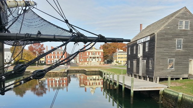 Several multi-story brick and wood-sided buildings line a waterfront reflected in the water. 