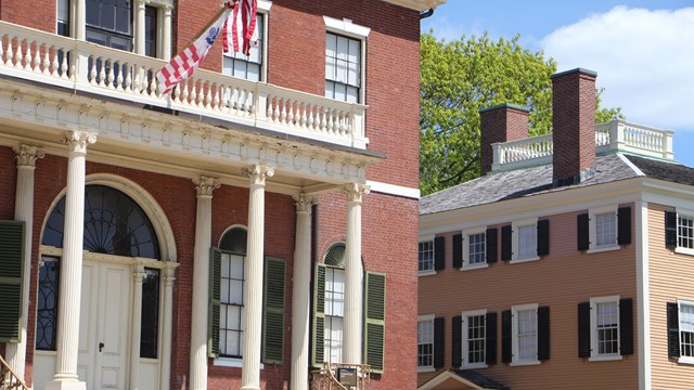 A three-story brick building with covered doorway next to a three-story, wood-sided yellow building.