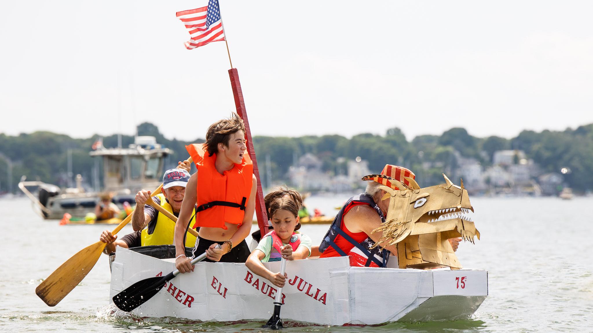 A group in a decorated cardboard boats race in a harbor