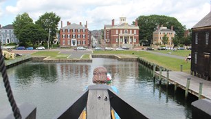 View over the bow, or front of a ship, with multi-story brick buildings across the water.