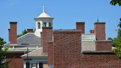Rooftops and brick chimneys of three historic buildings with white cupola atop the last.