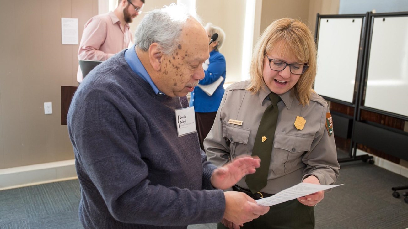 Two people speak to one another looking at a paper.