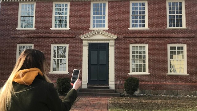 Woman and dog on a leash face away from the camera in front of a brick house. 