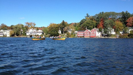 Two yellow boats on the water with homes visible on the shoreline. 