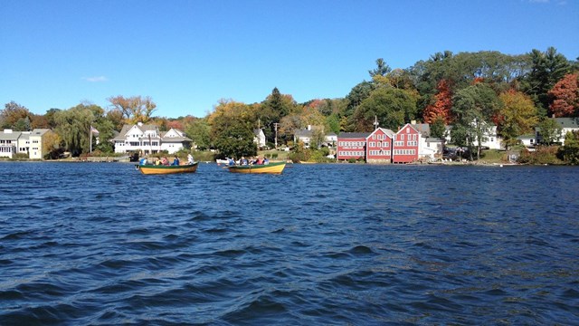 Two yellow boats on the water with homes visible on the shoreline. 