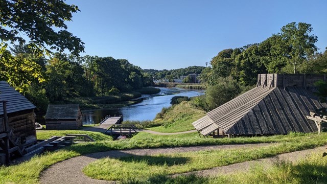 A paved path winds through several one-story, wood-sided buildings on a river.