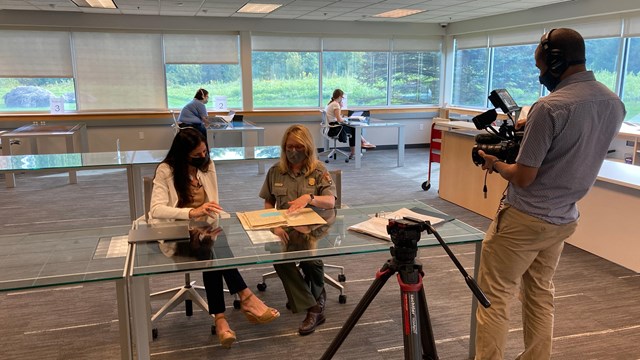 A man films to people sitting at a table. 