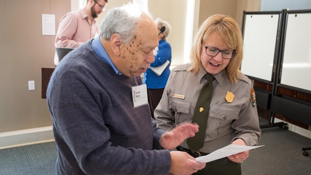 Park ranger and visitor examine document together. 