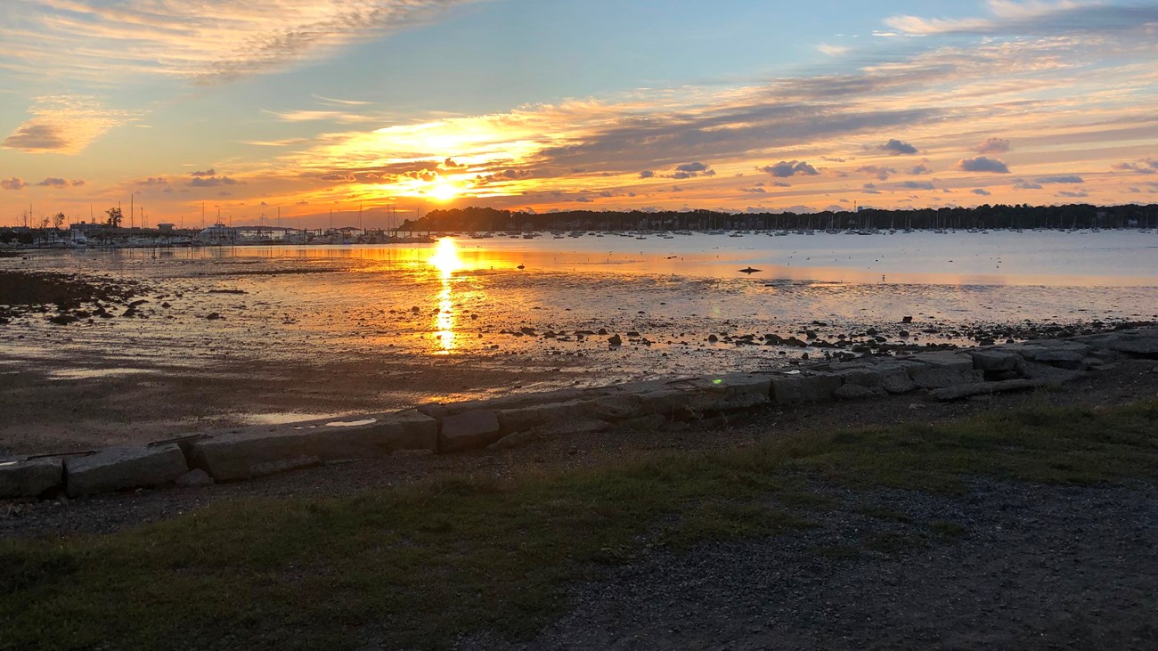 yellow sun rises over shallow water in a tidal harbor