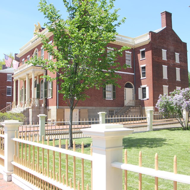 Two three-story historic buildings surround by grass and trees.