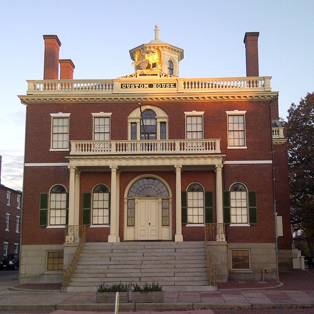 Two-story brick building with white columns and 12 steps leading to an arched doorway.