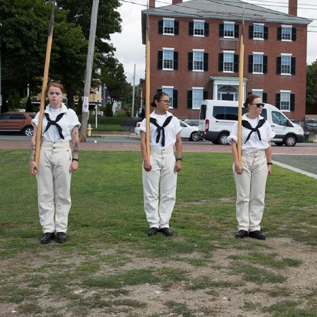 Three Navy women dressed in traditional sailor uniforms, white with blue sash ties.