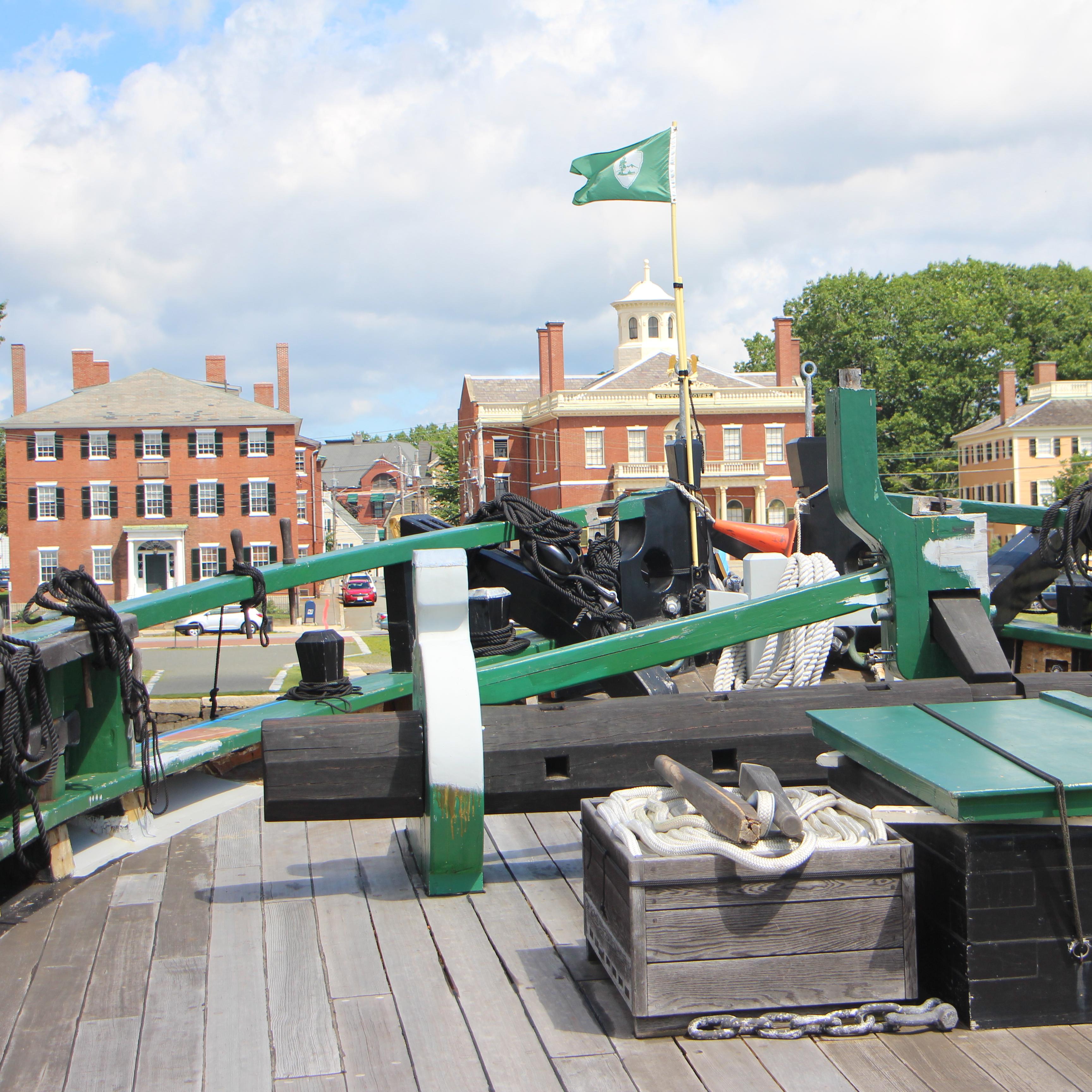 Ship deck with green rails and brick buildings on land.
