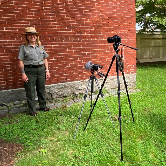 Two rangers prepare to film outdoors by setting up camera, microphone, and note cards.