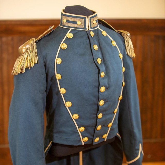 ii.	Grey military uniform adorned with golden buttons and golden shoulder pads with frills.