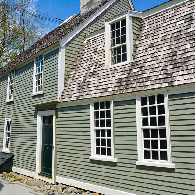 Side view of a two-story greenish-grey house with white trim