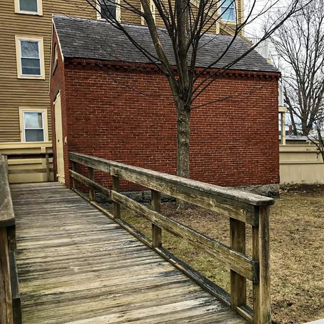 A wooden ramp leads to the side of a small brick building. 