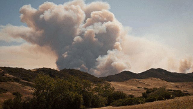 Billowing white smoke rising from green mountains.