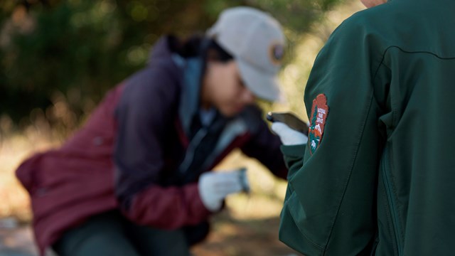 NPS jacket in focus with an intern working in the background out of focus.