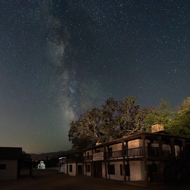 the milky way with historic buildings and trees being lit up in the foreground.