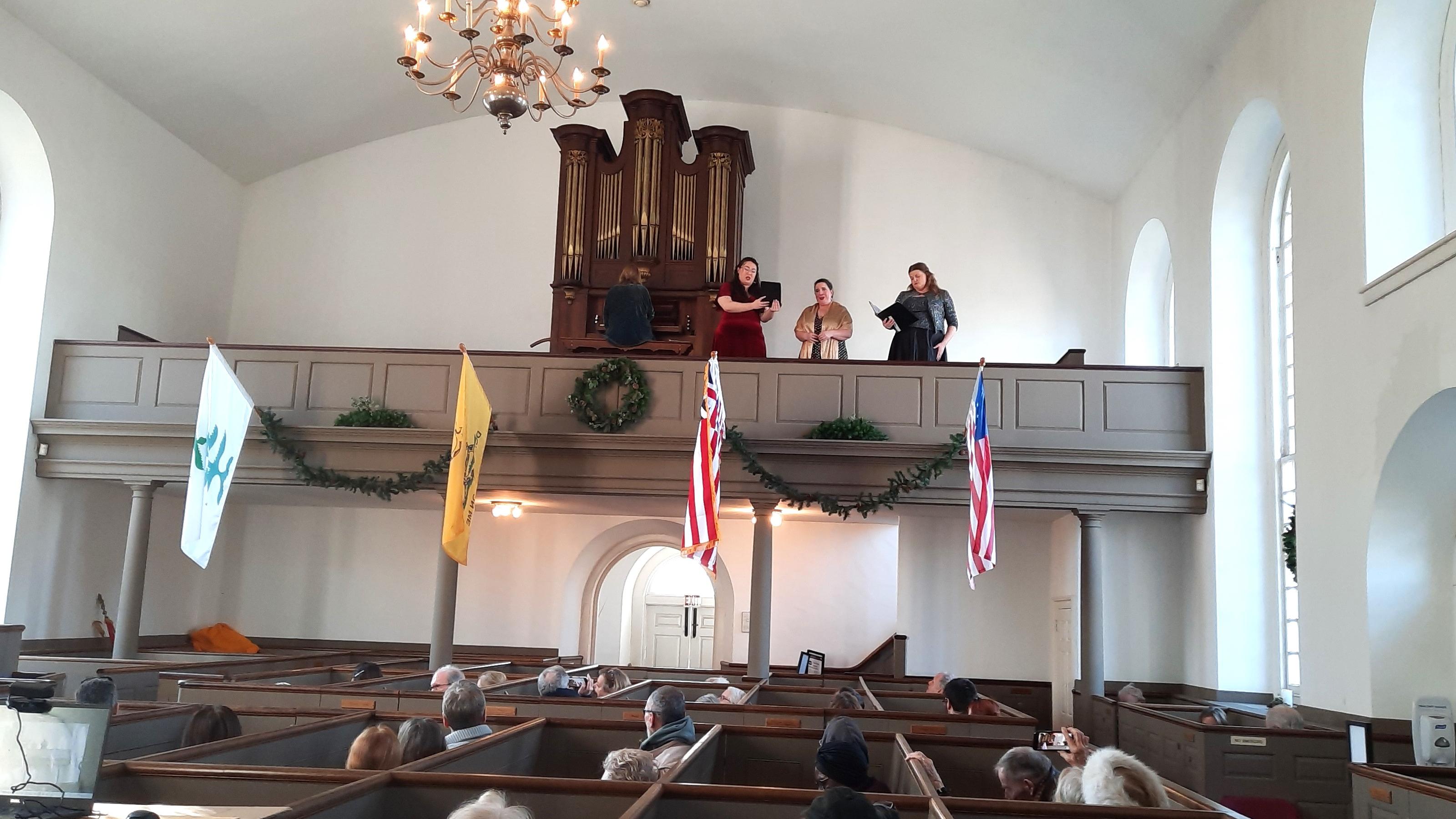 Color photo of a concert in a historic church, with singers and seated spectators visible. 