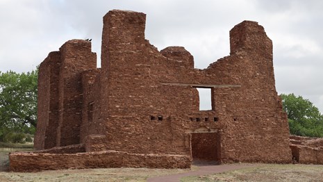 Front entrance of red sandstone church ruins against a cloudy sky background.