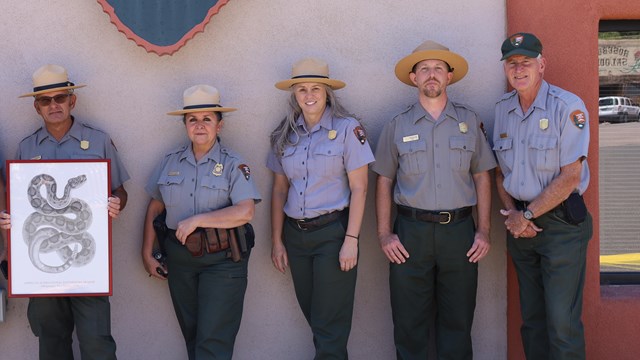 A group of five park rangers standing in front of a building.