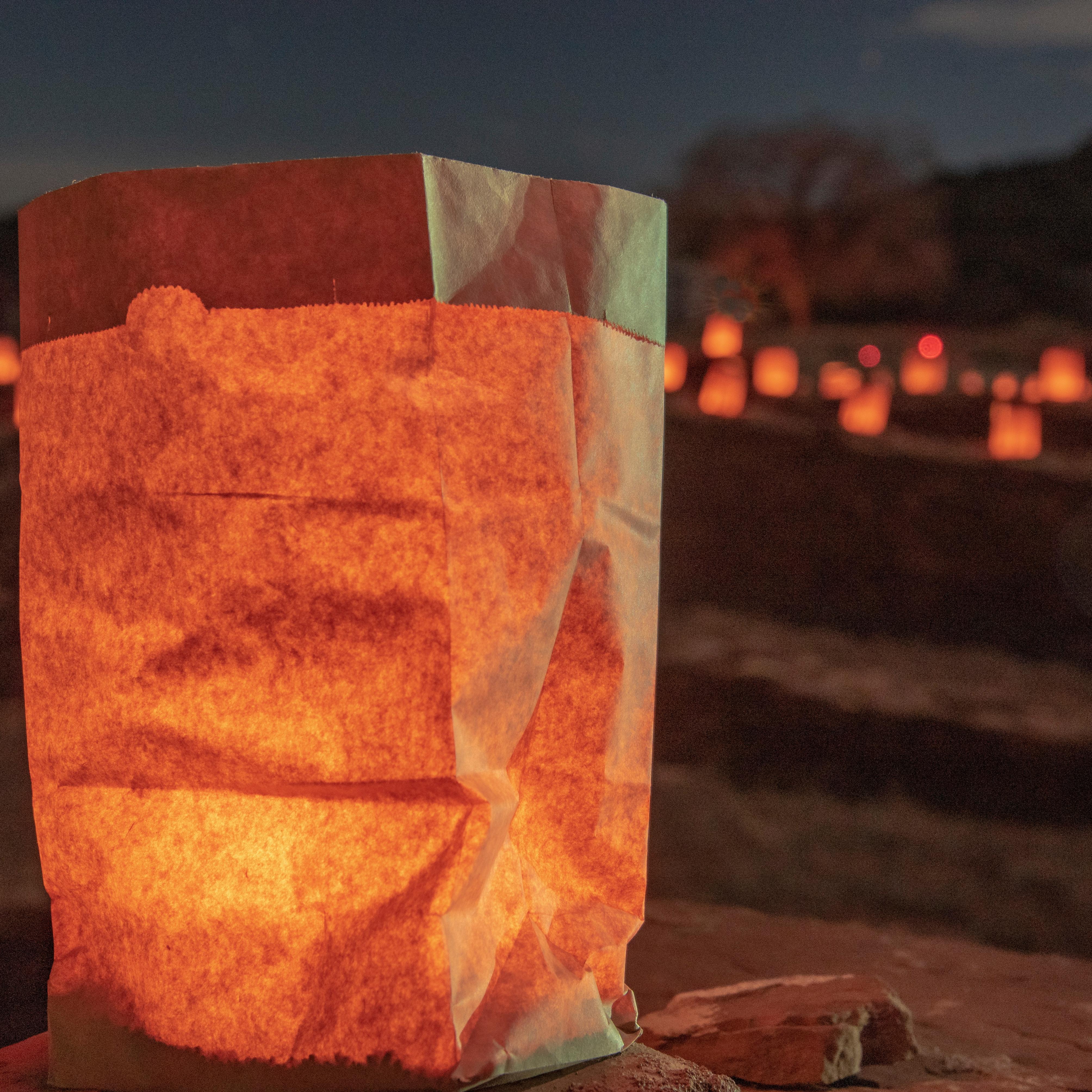 Luminaria on a stone surface with numerous luminarias softly illuminating a dark outdoor landscape.