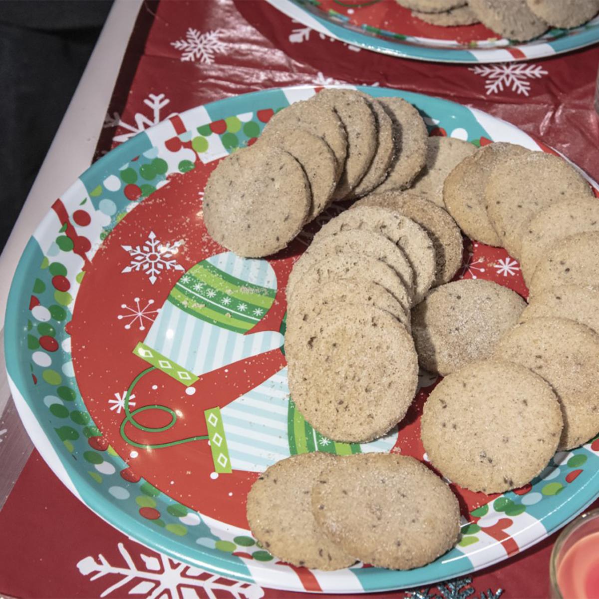 A festive Christmas-themed paper plate loaded with round, sugar-dusted cookies.