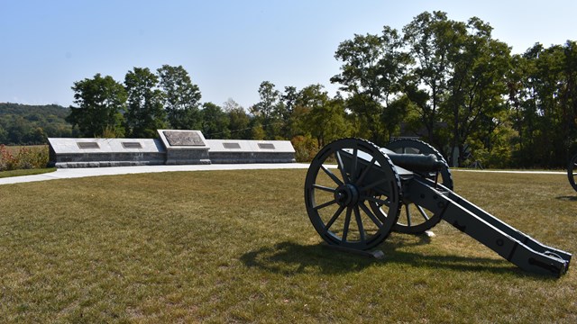 A canon on a grassy knoll in front of an informational exhibit outdoors