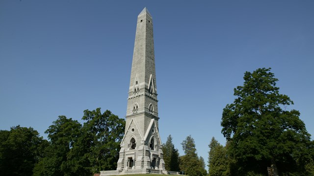 A tall gray obelisk on a grassy knoll.
