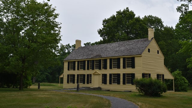 Large, yellow, two-story house surrounded by trees.